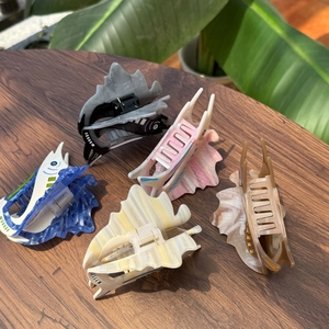 Detailed view of five fish-shaped acetate hair claws in various colors on wooden surface