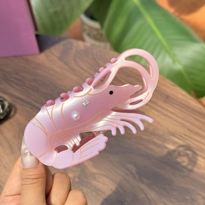 Pink shrimp hair claw clip with pearls and rhinestones on a natural wooden background