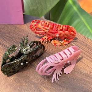 Top view of shrimp-shaped hair claws with pearls and rhinestones on a wooden table