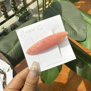 Barrette à cheveux ovale longue en acétate rose marbré sur fond de plantes vertes