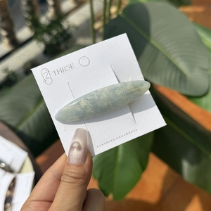 Barrette longue ovale en acétate marbré bleu et jaune sur carte devant un fond de plantes
