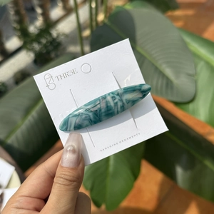 Détail d'une barrette longue en acétate avec texture marbrée verte sur carte de marque