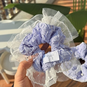 Lavender purple scrunchie with white lace edges and silver bow label held in hand
