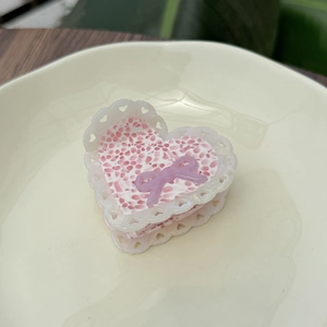 Pinza per capelli a cuore rosa con fiocco e pizzo traforato su piatto di ceramica