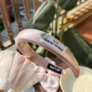 Detail eines rosa Glitzerstirnbands mit silbernem Blumenknopf und Stoffetikett