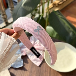 Detailansicht eines rosa geflochtenen Stirnbandes mit silbernem Schleifenanhänger am Tisch