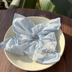 Nahaufnahme von blauem Karo-Haargummi mit weißer Spitze und Silberschleife auf Keramikteller