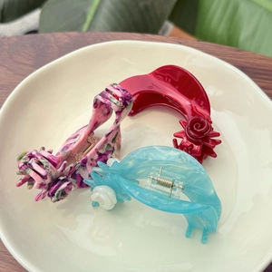 Detailed top view of three floral acetate hair claws with rose patterns in a ceramic dish