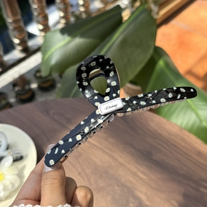 Detailansicht einer schwarzen Gänseblümchen-Haarklammer mit Blumenmuster und Daisy-Logo