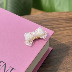 Elegant white lace bow acetate hair clip with golden metal duckbill base on a book