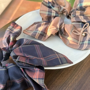 Blue and khaki plaid scrunchies with bow and pearl detail on a white ceramic plate