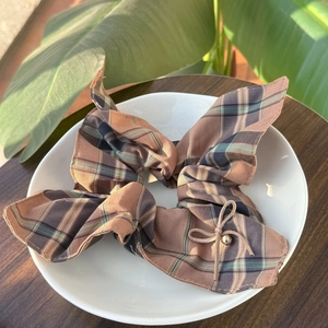 Brown plaid bow hair scrunchie with rabbit ear design and gold bead on white plate