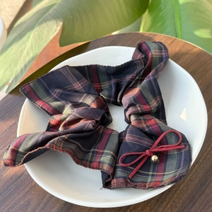 Plaid scrunchie with red bow and gold bead detail on a white ceramic plate