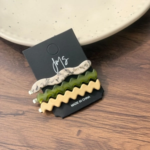 Vue détaillée de trois barrettes à cheveux ondulées en acétate, coloris gris, vert et crème