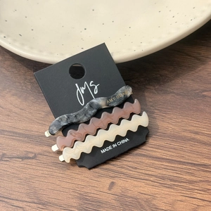 Gros plan de trois barrettes à cheveux ondulées en acétate, coloris marbre, café et beige