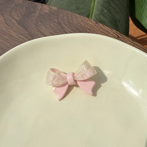 Pink and pearlescent acetate bow hair clip on a ceramic plate with natural lighting