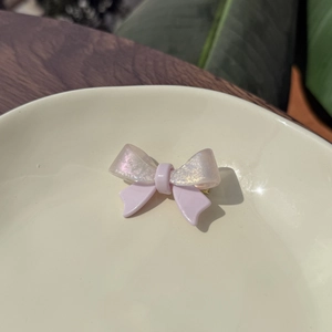 Pink acetate bow hair clip with shimmering glitter wings on a white ceramic tray