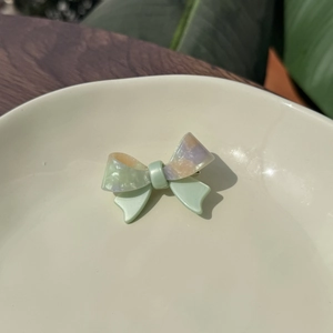 Detail of a handmade acetate bow hair clip in green with purple marble patterns