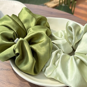 Close-up of olive and mint green satin scrunchies showing glossy fabric texture in a white tray