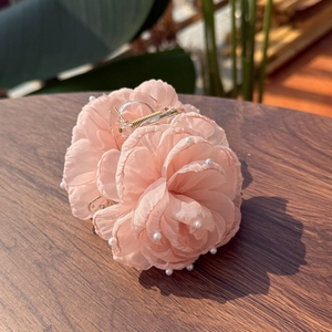 Pink fabric flower hair claw clip with white pearls and gold metal spring on a dark table