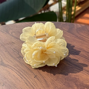 Elegant pale yellow chiffon flower hair claw clip with pearls on a wooden surface