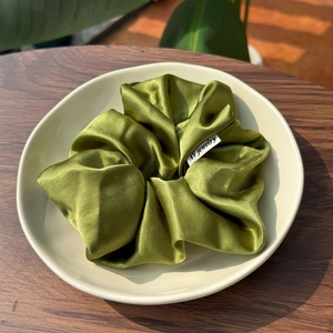 Forest green oversized satin scrunchie with silky finish on a decorative ceramic tray