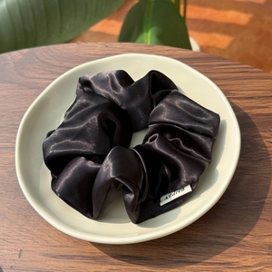 Elegant oversized black satin scrunchie with silk gloss finish on a ceramic plate