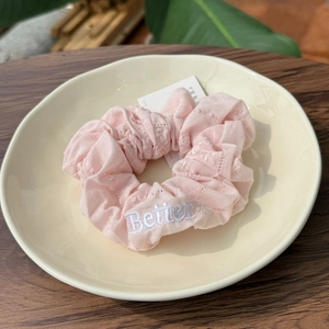 Chouchou rose avec broderie Better sur tissu texturé posé sur une assiette en céramique crème