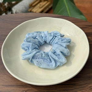 Gros plan d'un chouchou en tissu bleu clair avec broderie florale et lettres violettes