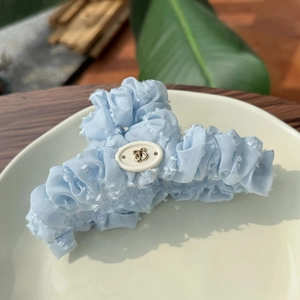 Détail de la pince à cheveux en tissu plissé bleu clair avec ornement papillon doré