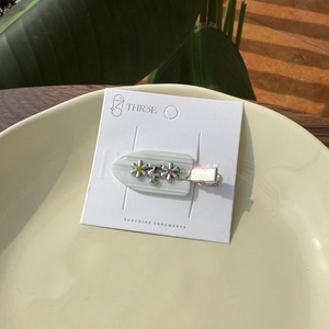 Détail d'une pince à cheveux en acétate avec fleurs et strass colorés sur un plateau chic