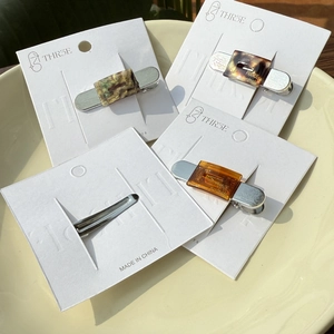 Set of four tortoiseshell acetate hair clips with silver metal base on a cream plate