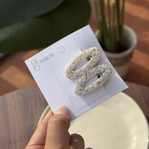Détail de la texture des pinces à cheveux ovales en acétate marbré beige et gris sur carte