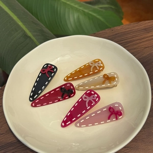 Detailed set of 6 colorful acetate hair clips with bow accents on a ceramic plate