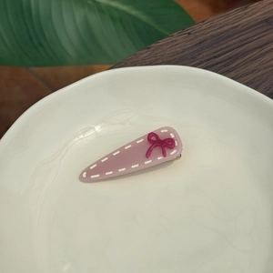 Close-up of pink acetate hair clip with burgundy resin bow on a white ceramic plate
