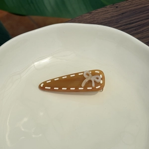 Amber acetate hair clip with white bow and stitching details on a white tray