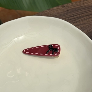 Macro shot of dark red acetate bow hair clip with white border on a cream porcelain plate