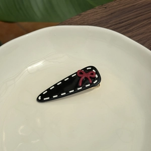 Detail of a black acetate hair clip with white stitching and a red bow on a ceramic plate
