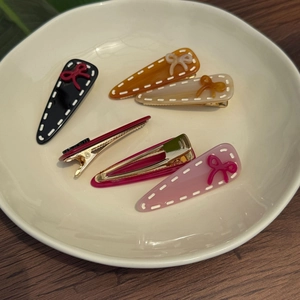 Set of five acetate hair clips with white stitch patterns and mini bows in a ceramic bowl