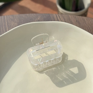 Iridescent square hollow hair claw clip made of acrylic on a beige ceramic plate