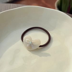Brown elastic hair tie with cream acetate heart pendant featuring a bow and rhinestone