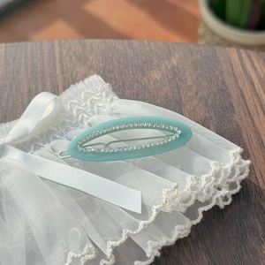 Detail of oval cutout hair clip with rhinestones on white lace and wood background
