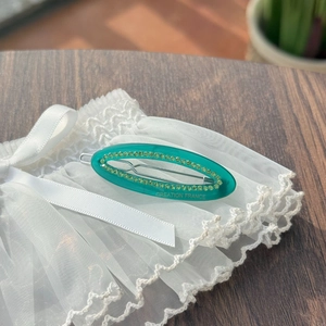 Detailed view of an oval green acrylic hair clip with rhinestones on a wood background