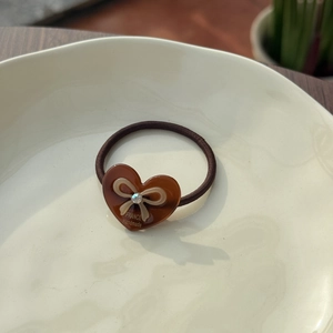 Close-up of a heart-shaped acetate hair tie with bow relief and a sparkling rhinestone
