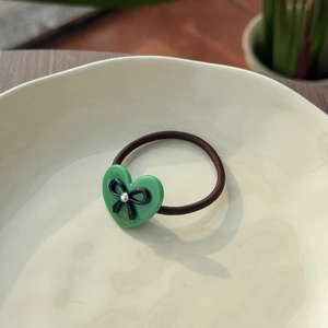 Detail of a brown elastic hair tie featuring a green acetate heart with a black bow and crystal