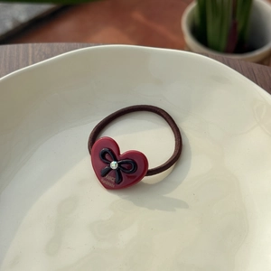 Close-up of a red acetate heart charm with a black bow and crystal on a brown hair tie