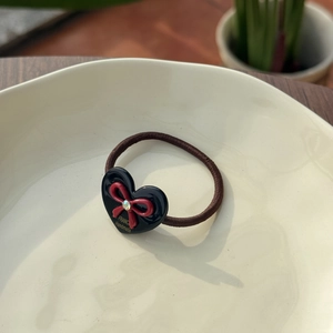 Detail view of heart acetate hair tie with red bow and crystal in cream dish