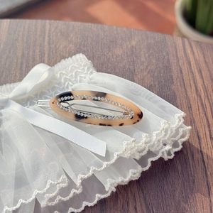 Detail view of oval tortoise shell hair clip with rhinestones on lace and wood surface
