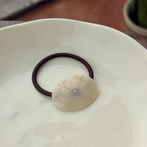 Close-up of cream oval acetic acid hair scrunchie with gold grid dots and rhinestones