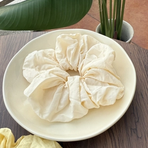 Minimalist ivory scrunchie with soft fabric texture on a ceramic plate for hair styling